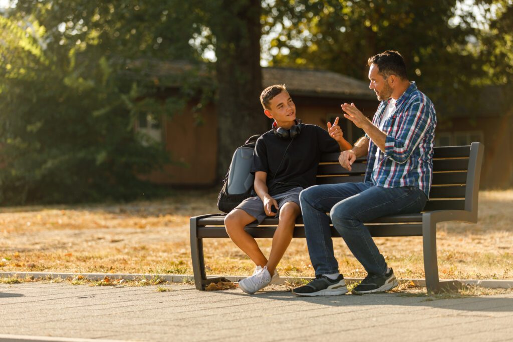 father and teenage son casually chatting on the street bench